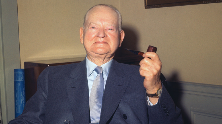 An elderly Herbert Hoover holding a pipe in his office