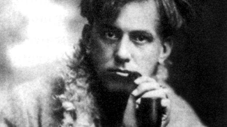 Aliester Crowley holding smoking pipe looking serious