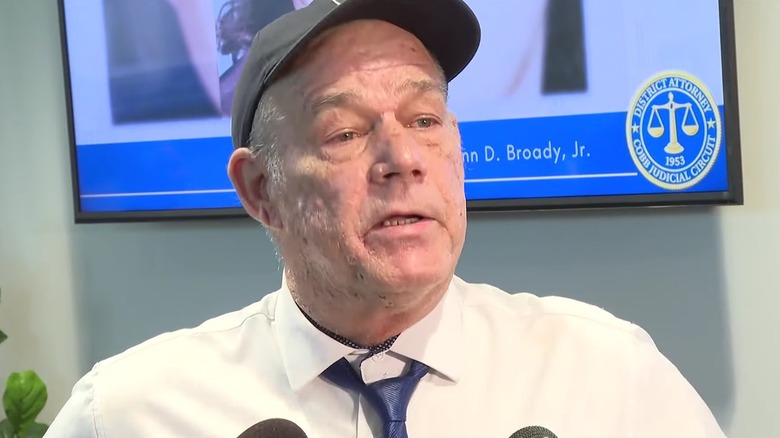 Man hat white shirt speaking at press conference