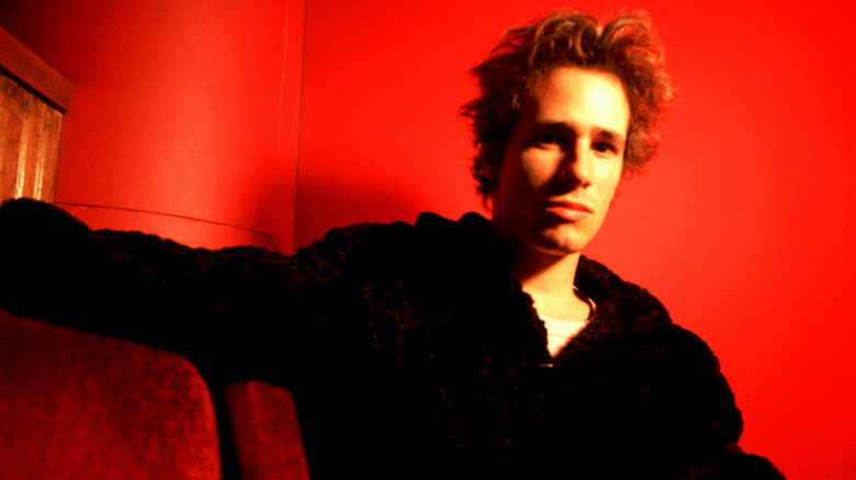 Jeff Buckley stares at the camera while sitting on a couch in a red room