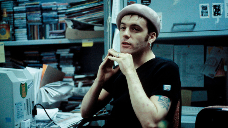 Richey Edwards sits at a desk in a room with CDs in the background