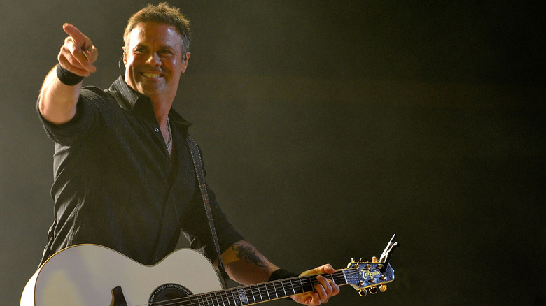 Troy Gentry smiles and points at the crowd while playing guitar on stage