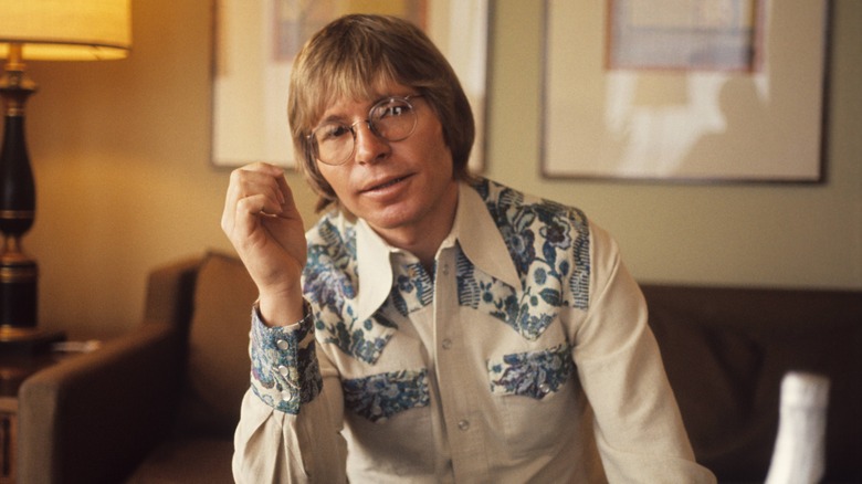 John Denver glasses seated indoors