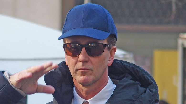 Edward Norton blue cap sunglasses raising arm