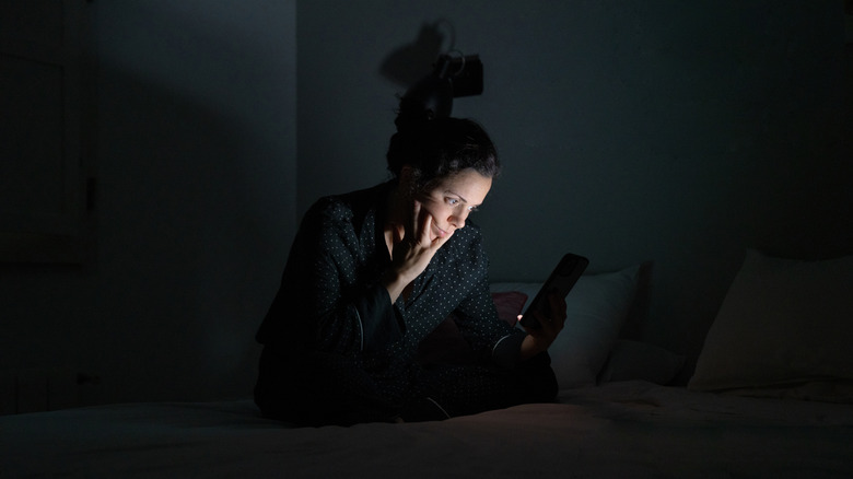 Sad woman using cellphone in dark 