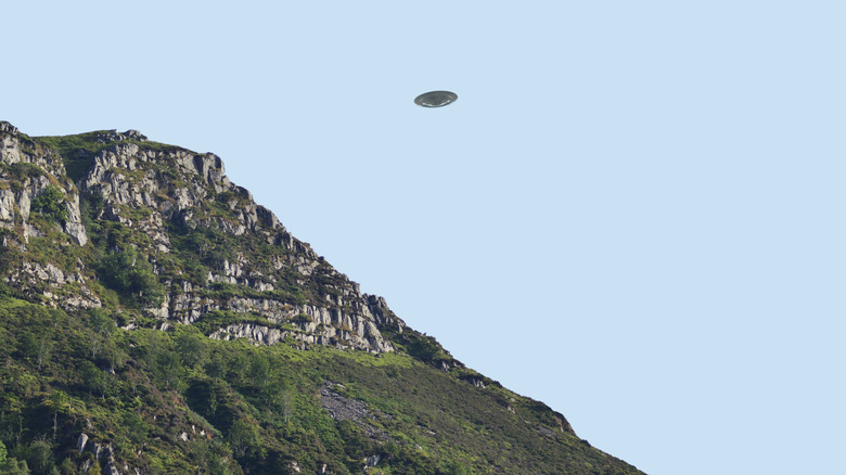 Flying saucer UFO over bluff/ cliff side in summer, clear blue sky background, CGI recreation