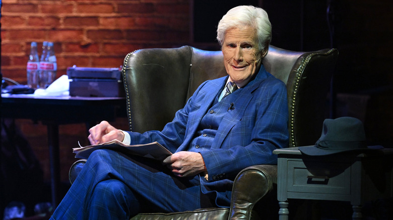 Keith Morrison on stage in leather armchair blue suit