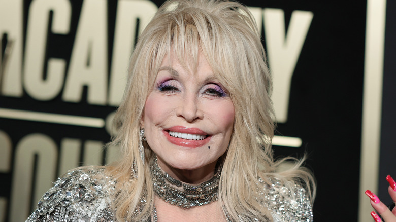 Dolly parton smiling in front of an Academy of Country Music sign