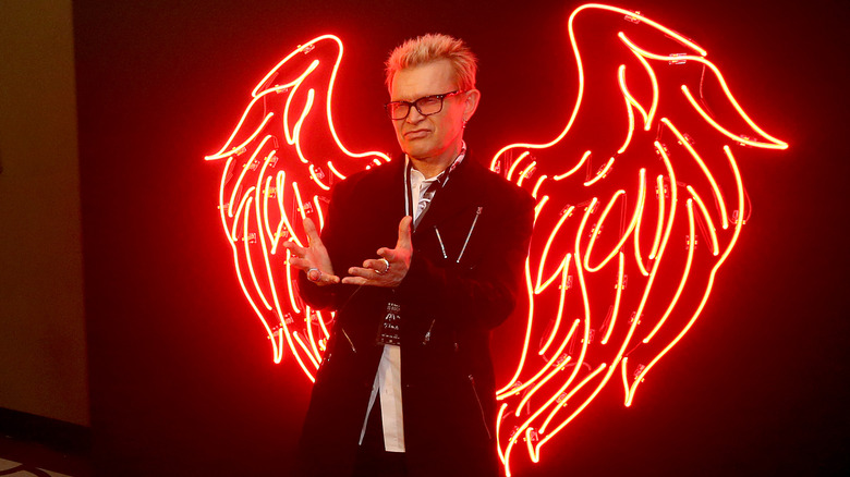Billy Idol posing in front of red neon angel wings