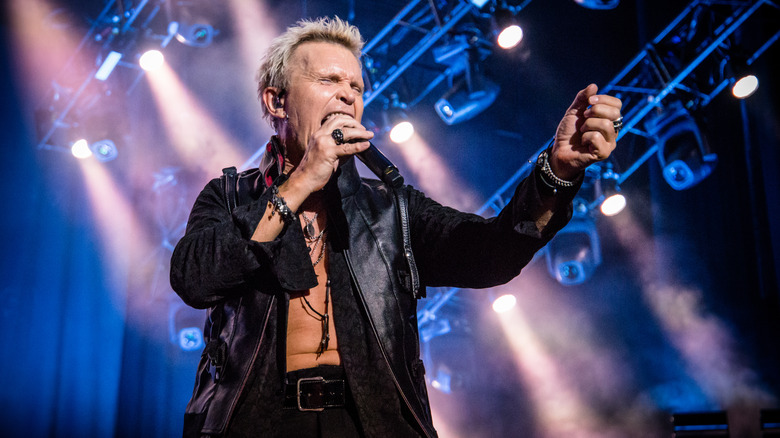 Billy Idol on stage singing holding mike black leather jacket