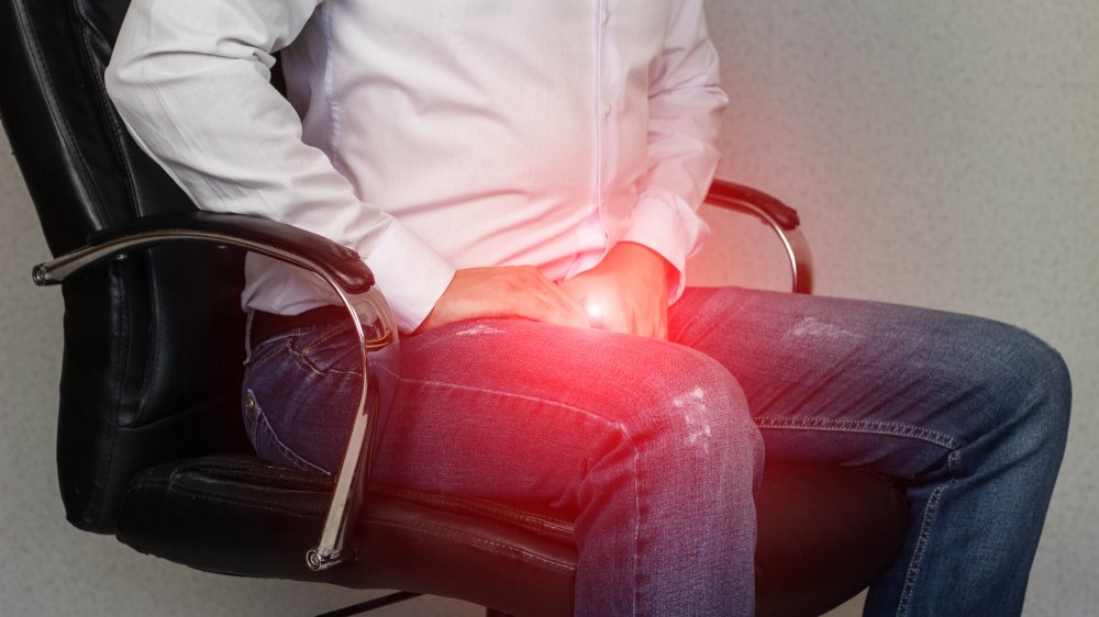 A man sits in an office chair and holds on to his groin,