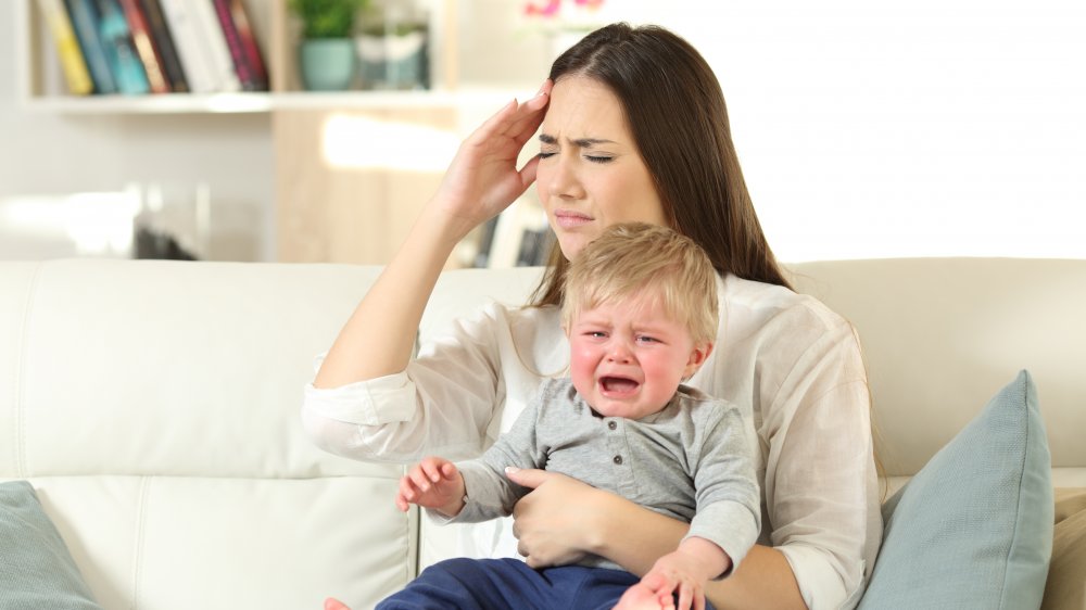 Mother suffering and baby crying desperately sitting on a couch in the living room at home