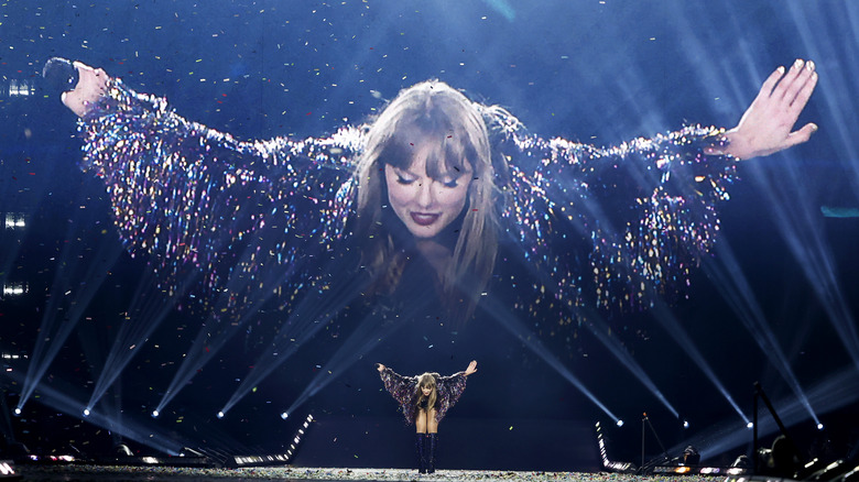 Taylor Swift bows, her bow enlarged on a projector behind her