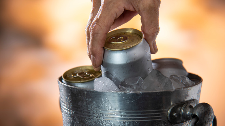 a hand pulling a can out of a bucket of ice