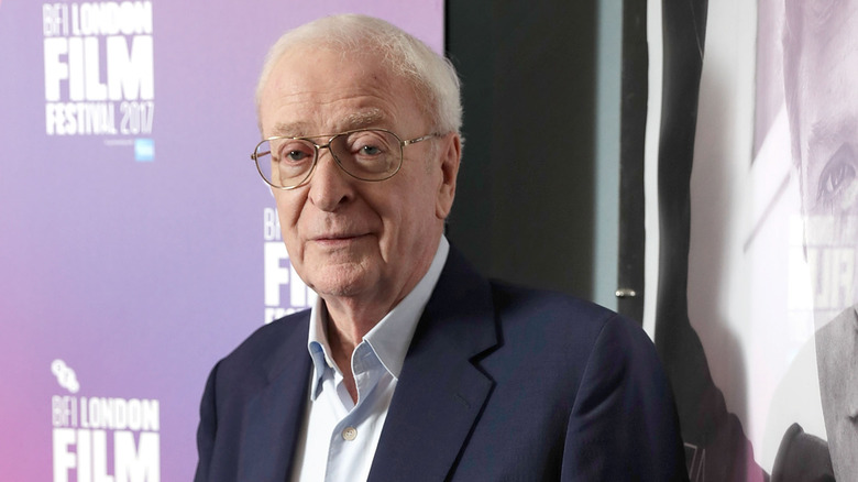 Michael Caine in front of a movie poster