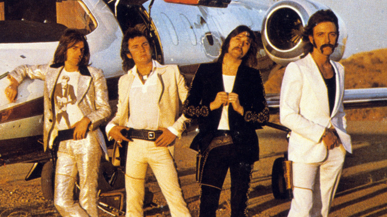 Foghat stands by a plane in 1970s publicity photo