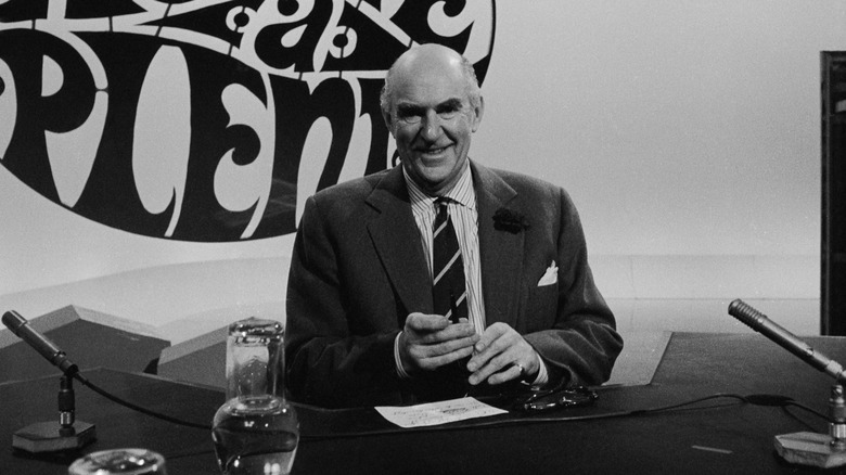 Kenneth Horne smiling suit sat at desk