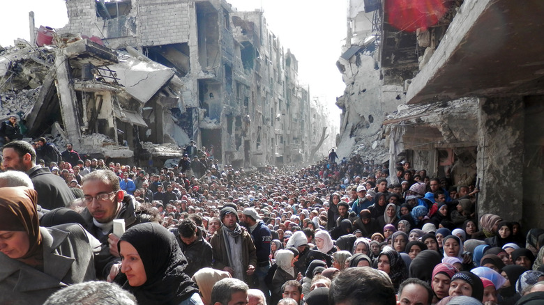crowd wait for food rations Damascus syria destroyed buildings