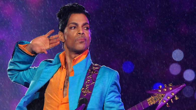 Prince blue jacket orange shirt cupping hand to ear guitar