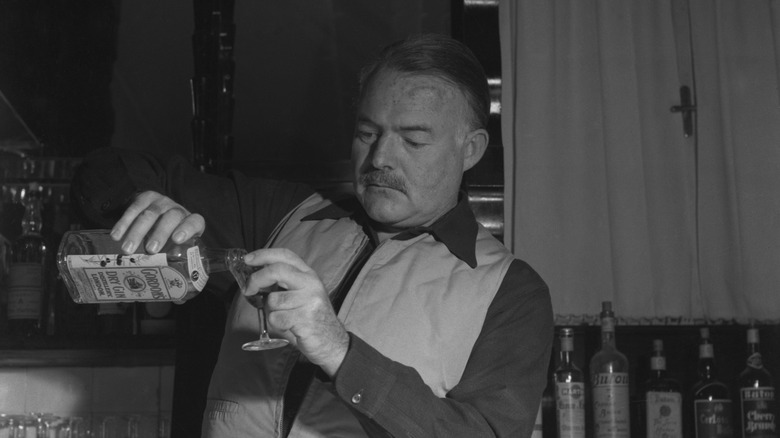 Hemingway in waistcoat pouring drink