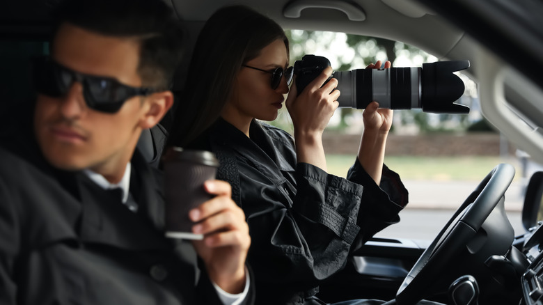 a man and a woman sitting in a car wearing sunglasses while the woman takes photos