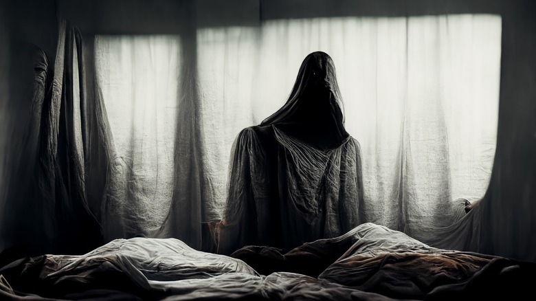 Hooded figure stands over bed