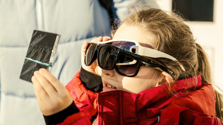 A child uses eclipse glasses and a filter