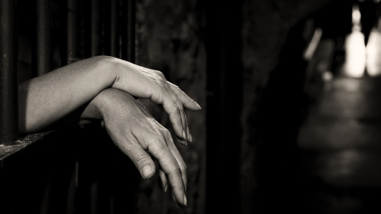 Women's hands draped over prison bars