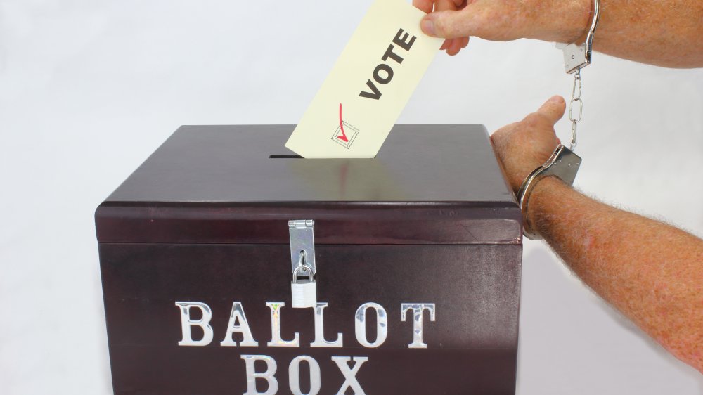 Handcuffed hands dropping a ballot into a voting box