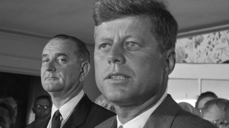 LBJ frowns behind JFK