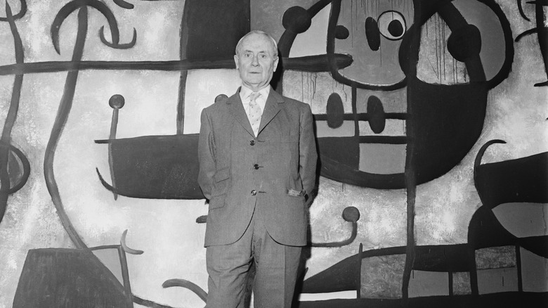 Joan Miro standing in front of his art