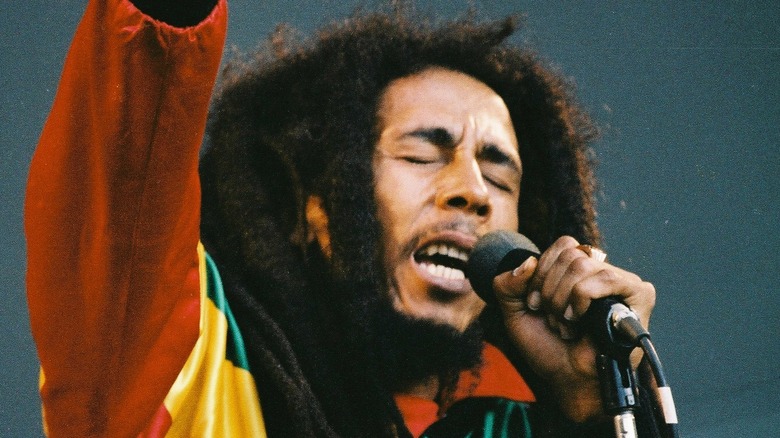 bob marley holding out arm while singing on stage with eyes closed