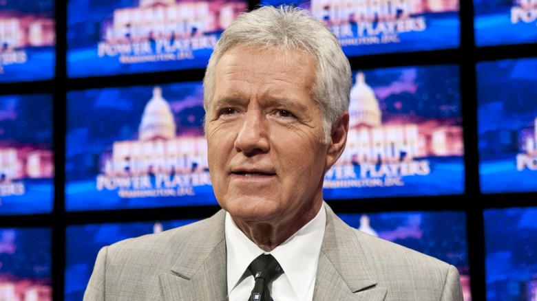 Alex Trebek smirking in front of Jeopardy board