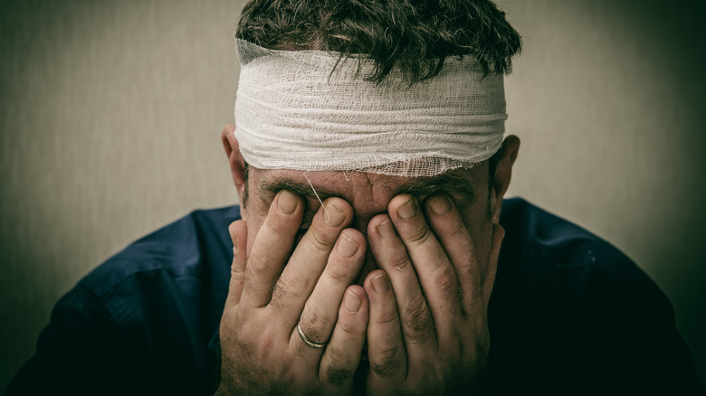 Man with bandage around head covering face with hands