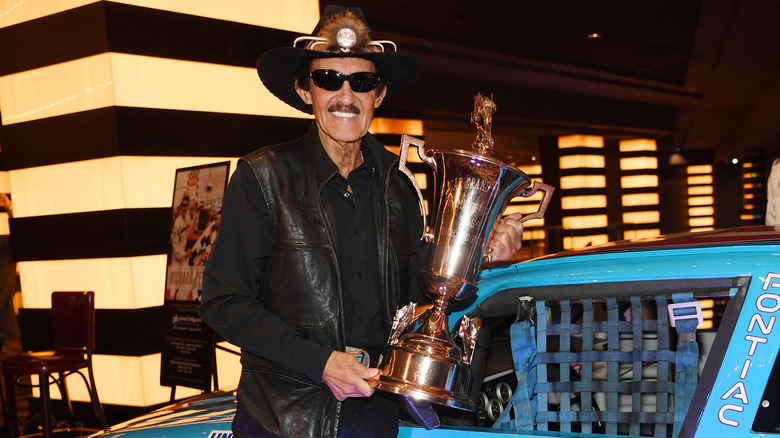 RIchard Petty holding a trophy by his car