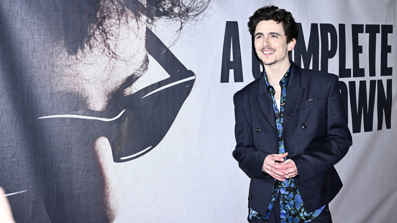 Timothee Chalamet posing in front of poster for A Complete Unknown