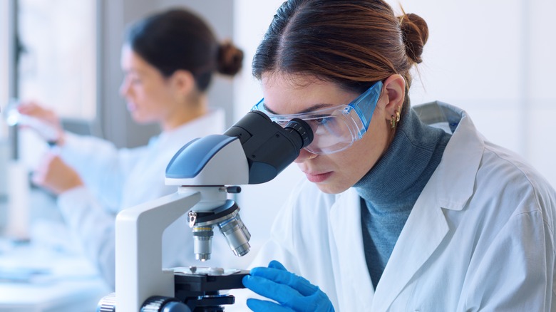 Scientists in lab safety goggles using microscope