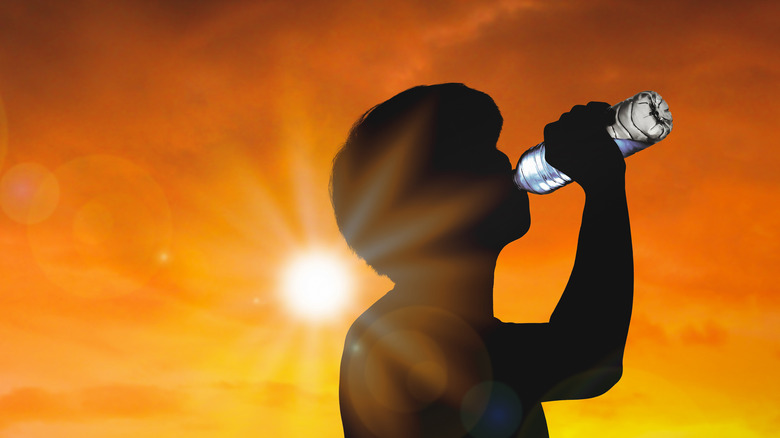 Man in silhouette drinking water with sun in background
