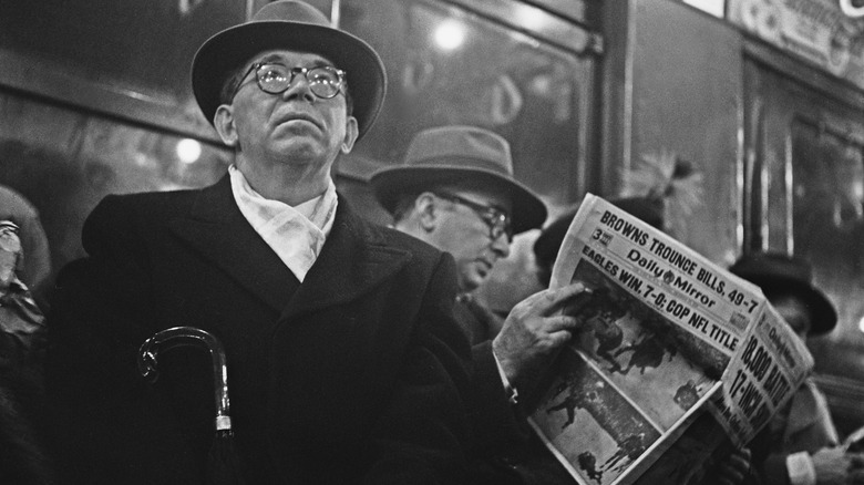 Two men sitting on a train, one holding a newspaper proclaiming the Eagles' vistory