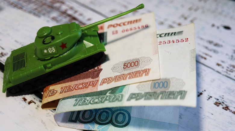 a toy tank running over Russian money