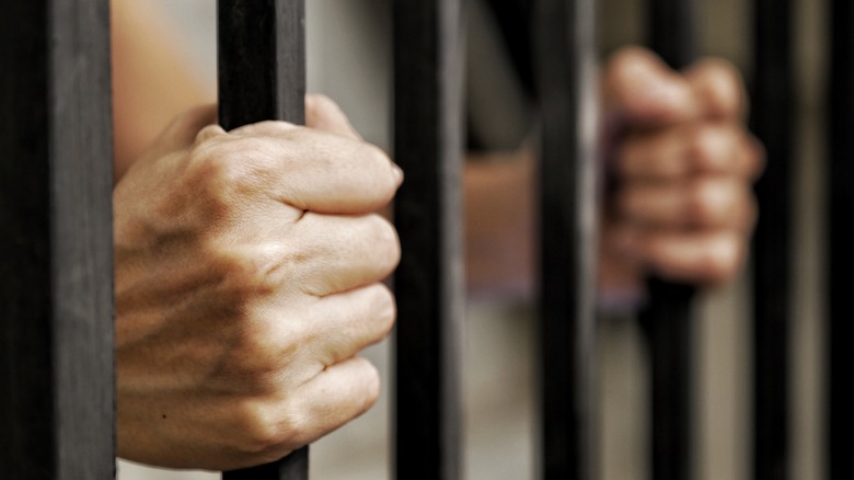 Hands of an inmate holding prison bars 