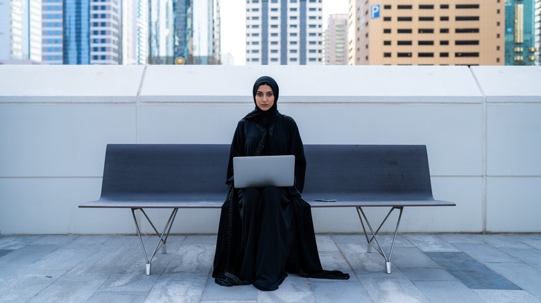 muslim woman sitting on a bench with laptop