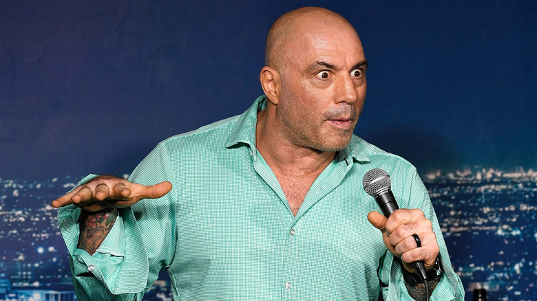 Joe Rogan gesturing while speaking into a microphone onstage