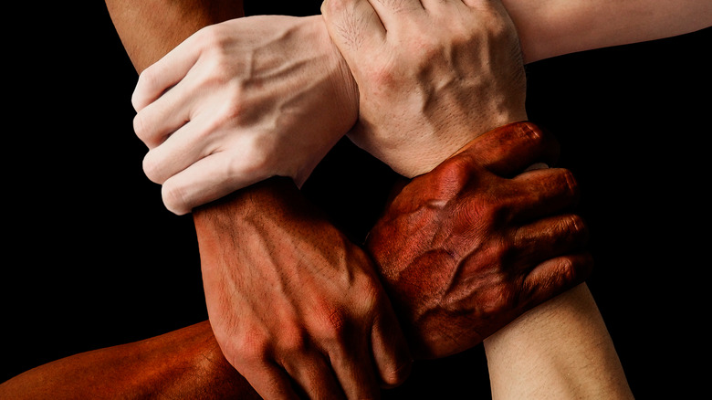 Four clasped hands with differing skin tones.