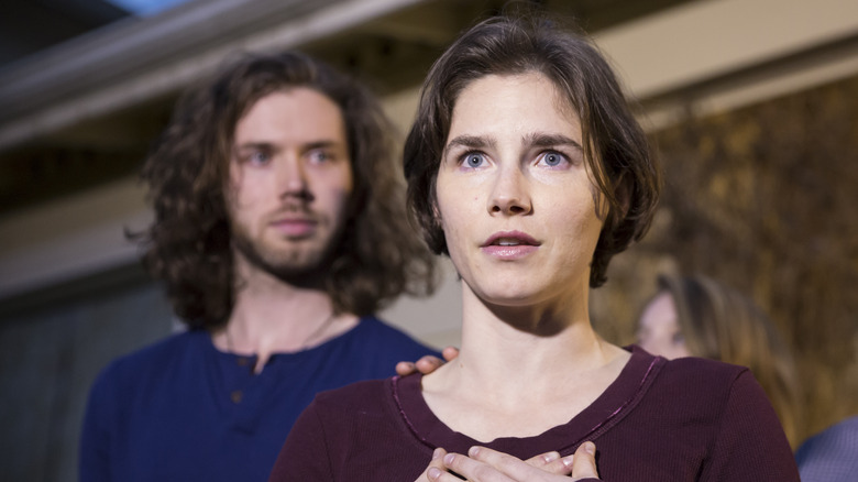 Amanda Knox crosses her hands while wearing a maroon sweatshirt.