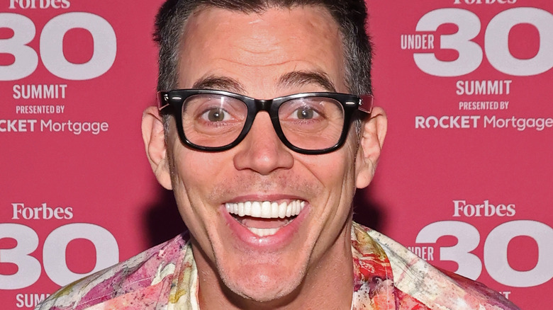 Steve-O wide smile thick glasses red background