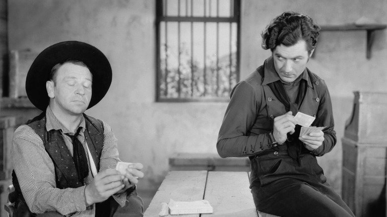 Actors portraying Pat Garrett and Billy the Kid playing cards in 1930 film