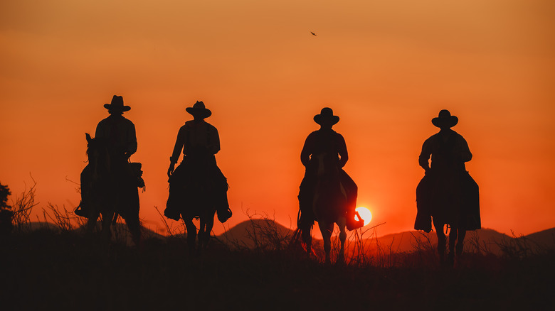 cowboys on horseback silhouetted by sunset