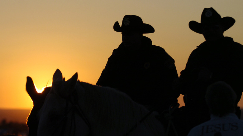 Two sheriffs deputies on horseback watch the setting sun 