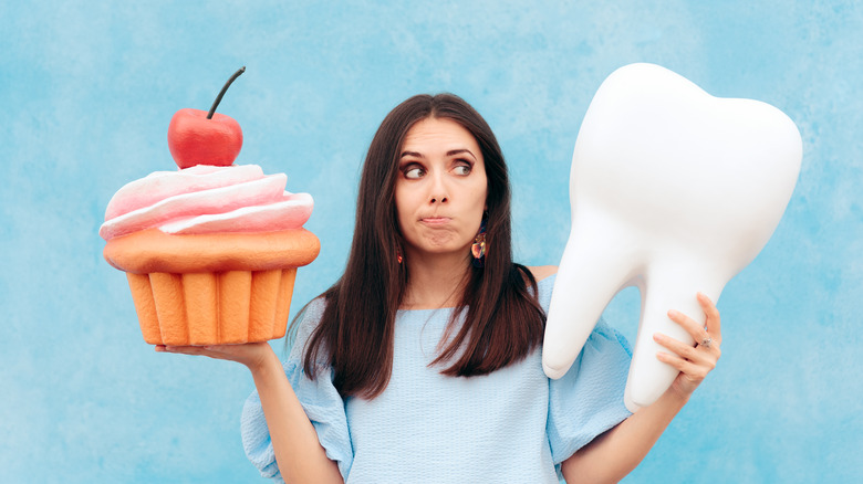 Person holding oversized sugary cake in one hand and oversized tooth in the other